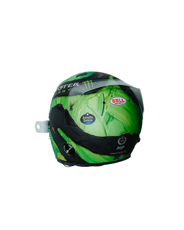 A green-and-black McLaren Lando Norris Monster Energy racing 1:5 mini-helmet with a clear visor, featuring sponsor logos including Bell and Sinter Series, photographed against a light gray background.