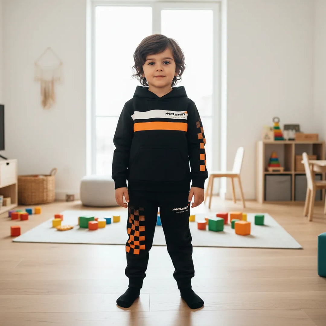 Child wearing a McLaren F1 Team Hoodie and Sweatpants Kids' Youth Set in Black with orange and white accents in a room with toys on the floor.