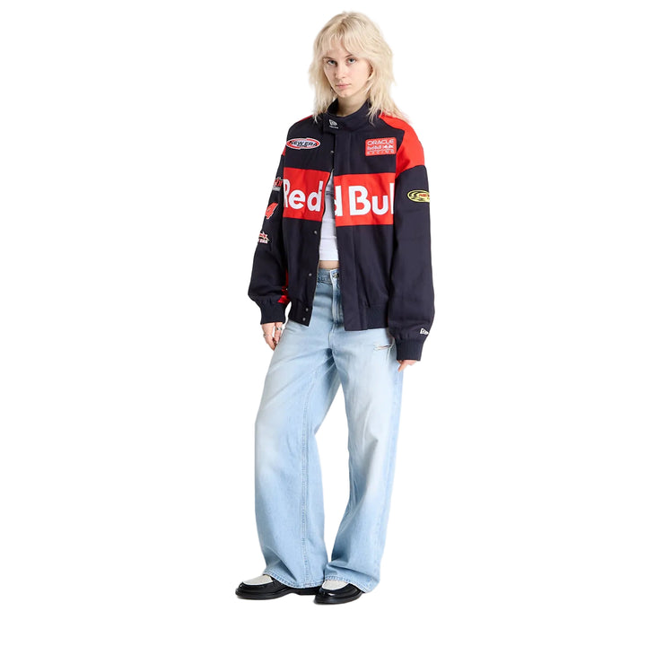 Full-length studio image of a woman wearing the black Red Bull Racing F1 motorsport jacket with light blue jeans.