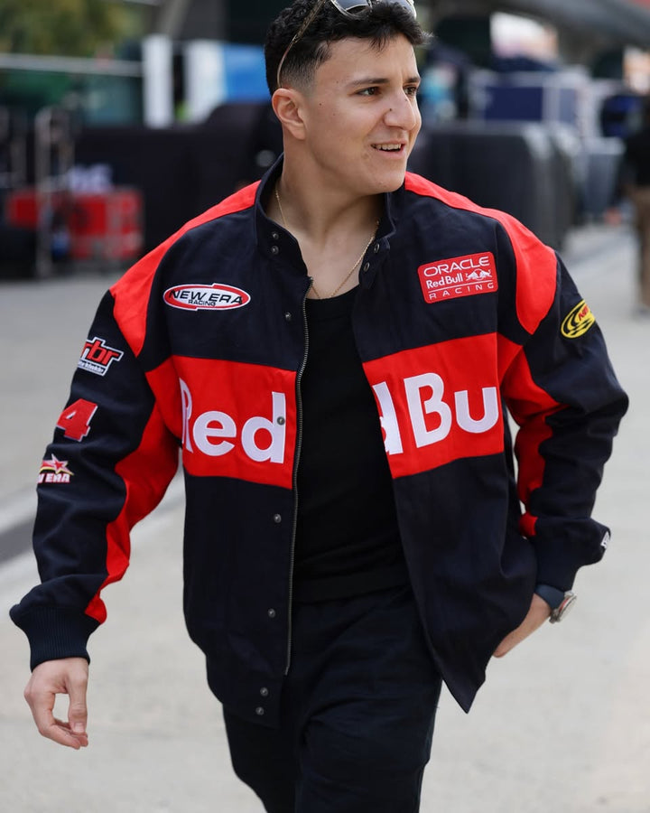 F1 Paddock garage trackside lifestyle photo of a Isack Hadjar wearing the blue Oracle Red Bull Racing New Era motorsport IH6 jacket with red team graphics.
