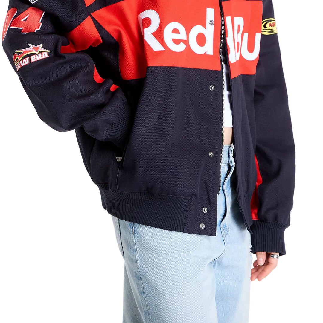 Detailed view of the snap-button front closure, red Red Bull chest graphic and black fabric on the New Era racing jacket.