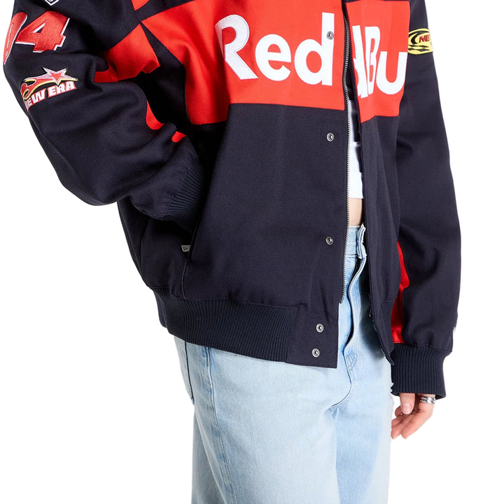 Detailed view of the snap-button front closure, red Red Bull chest graphic and black fabric on the New Era racing jacket.