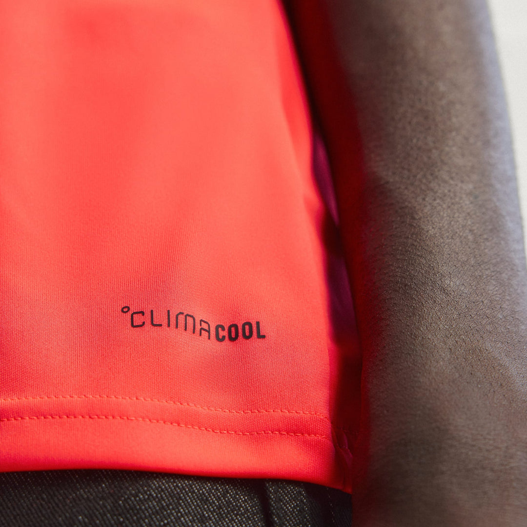 Close-up of a bright coral-orange AUDI REVOLUT F1 TEAM SET UP UNISEX TEE athletic fabric with a black adidas &