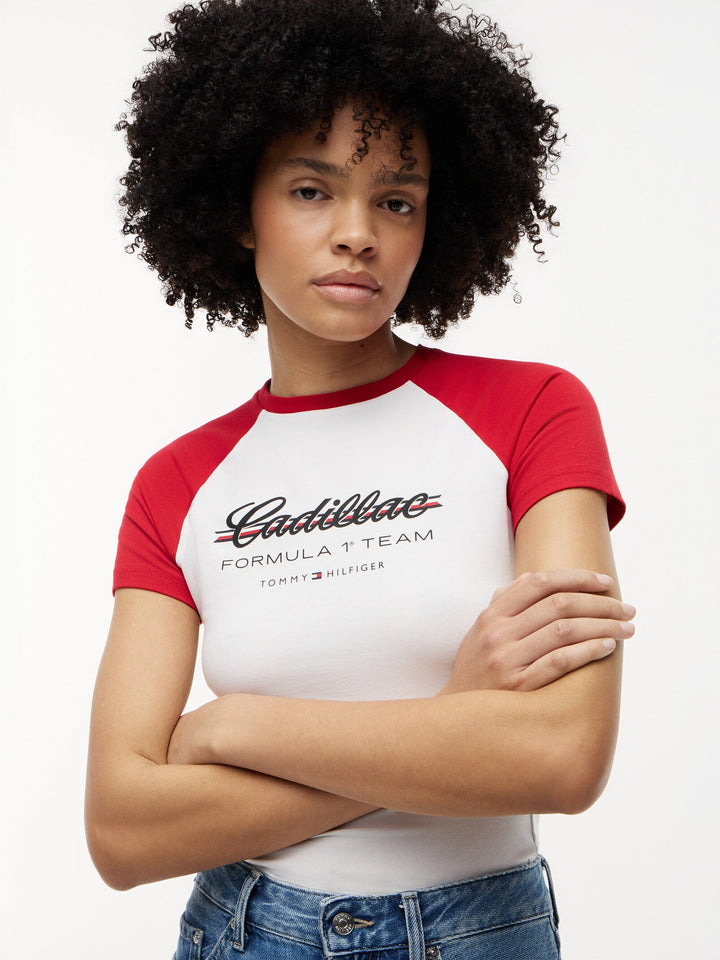 Cadillac F1 Team Female Race Fan wearing a red and white raglan fitted t-shirt with a large Cadillac x Tommy Hilfiger official logo on the chest on a white background