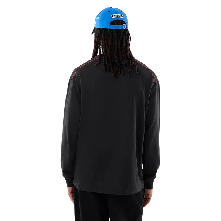 A person shown from the back wearing a black Authentic Williams F1 2026 Las Vegas Grand Prix Long Sleeve Shirt with red shoulder stripes, a bright blue Williams Racing Las Vegas GP limited edition cap, and black pants, photographed against a light gray studio background.