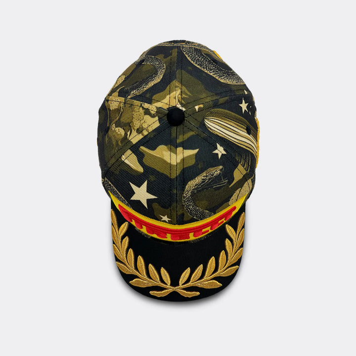 A Pirelli F1 Austin GP2026  cap featuring a dark green and black camouflage pattern with gold and white snake, star, and cloud motifs on the crown, and a black visor embroidered with a gold laurel wreath and a red and gold striped band.