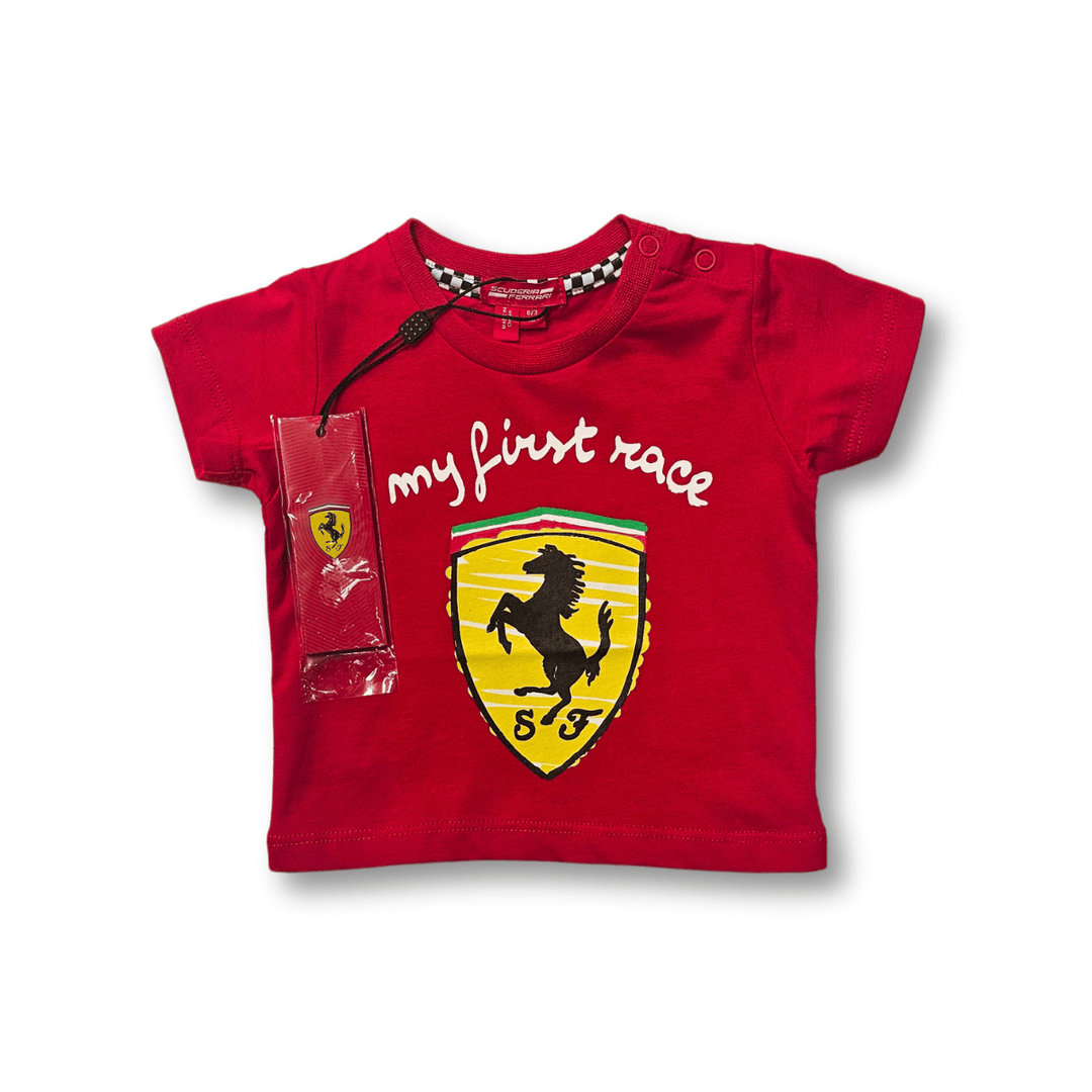 A red Scuderia Ferrari baby T-shirt in red with a white 'My First Race' text and the iconic Ferrari shield logo on the front. 