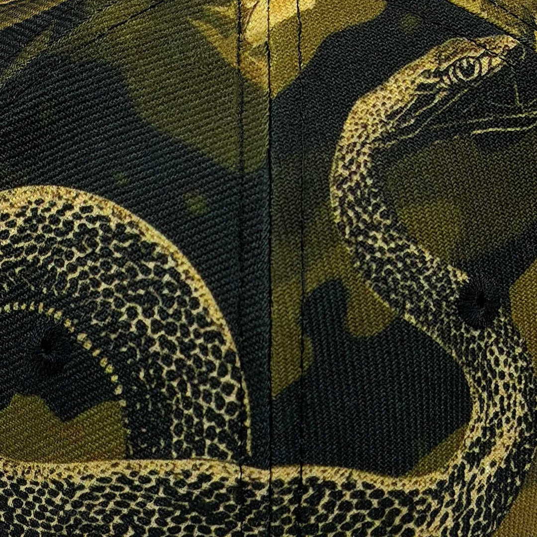 Close-up of a Genuine Pirelli Austin F1 2026 Podium Cap printed fabric featuring a coiled snake over a dark camouflage background in olive green, black, and tan.