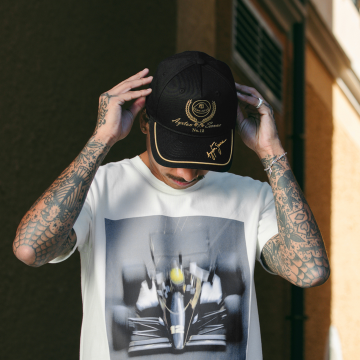 Ayrton Senna Team Lotus F1 black and gold cap shown in motorsport lifestyle setting