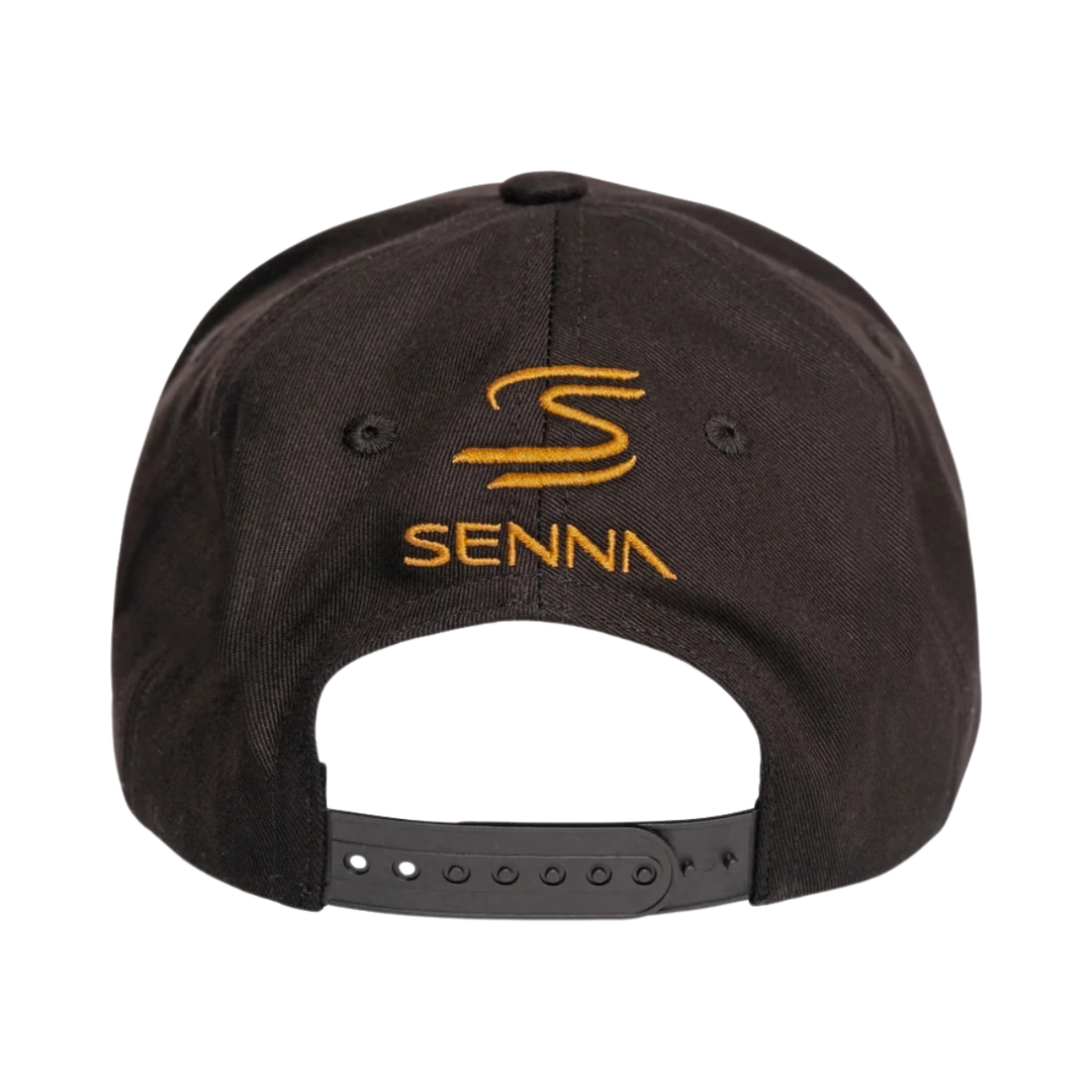 Ayrton Senna Team Lotus No. 12 cap close-up showing black and gold embroidered crest and signature
