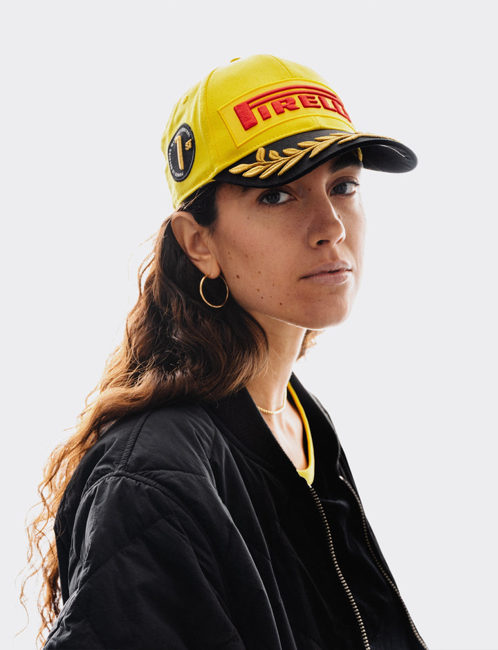 Female boasting the Limited edition Pirelli podium cap for the 2026 China Formula 1 Grand Prix in signature yellow with red logo patch, black visor, and gold laurel embroidery.