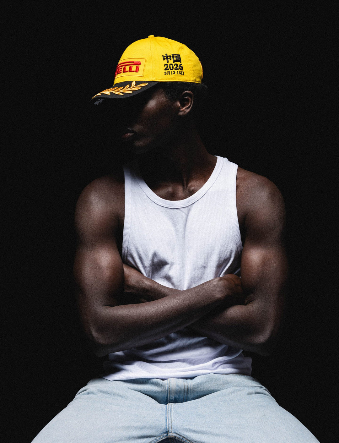 Coloured Male Model showing the left panel of the Official Pirelli F1 2026 Chinese Grand Prix podium cap in racing yellow with embroidered Pirelli logo, black brim, gold victory laurels, and race date marking.