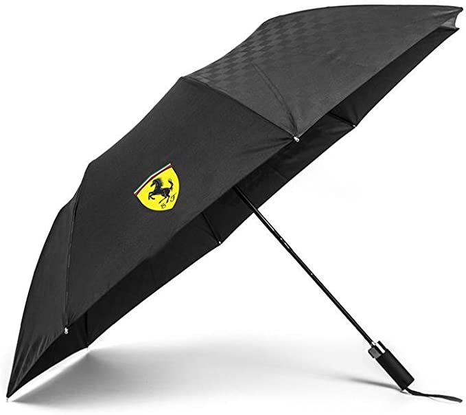A black Ferrari F1 Team compact umbrella with the Scuderia Ferrari Formula 1 team branding, including the signature prancing horse logo, displayed when opened. The umbrella is shown with a carrying case/sleeve.